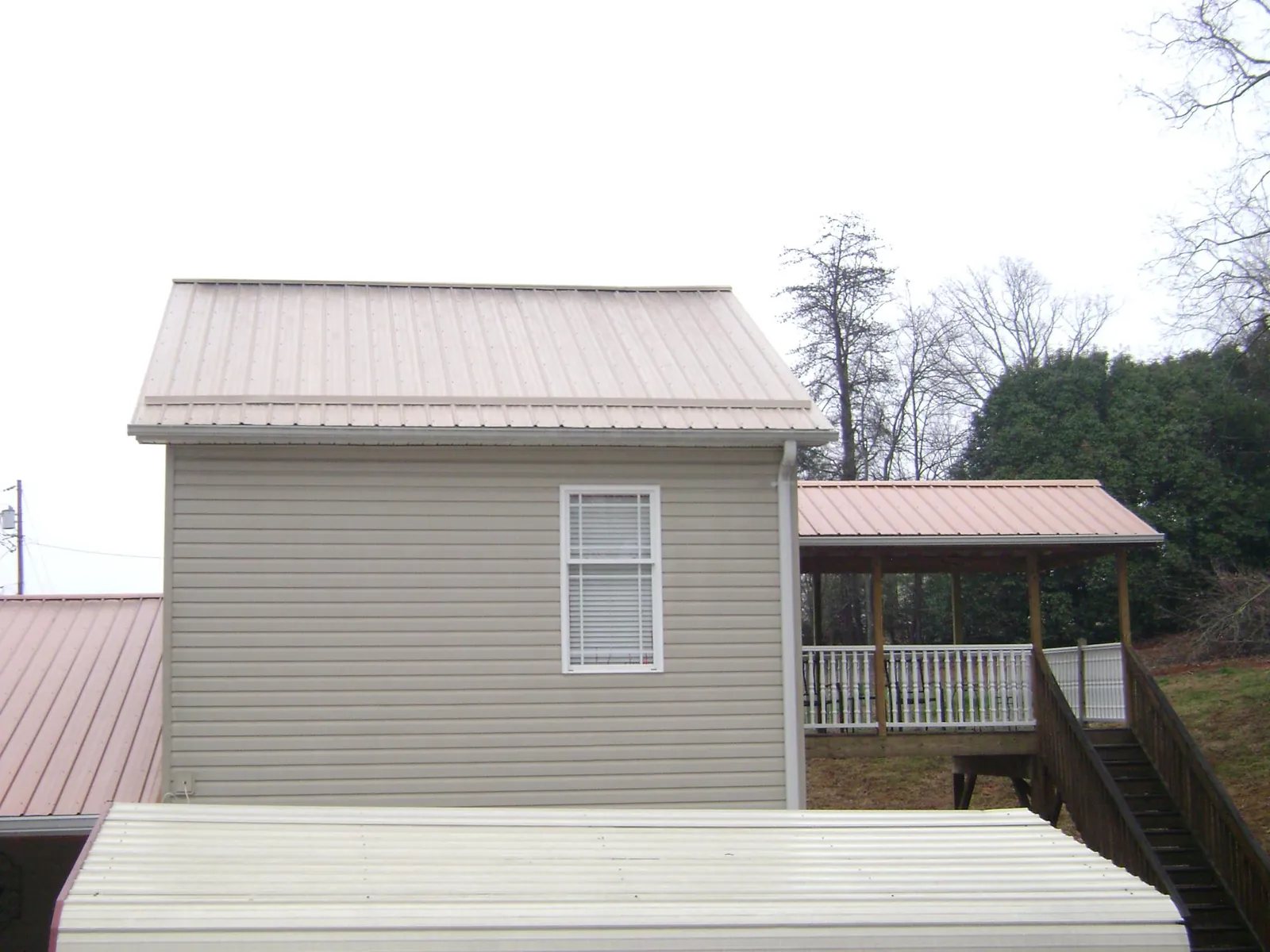 Tan metal roofs on a two story addition and attached porch, from a Roof Replacement job in Marshall